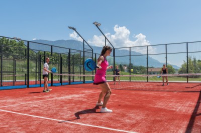 Quatre personnes jouent au padel sur un court extérieur avec vue sur des montagnes et un ciel dégagé.