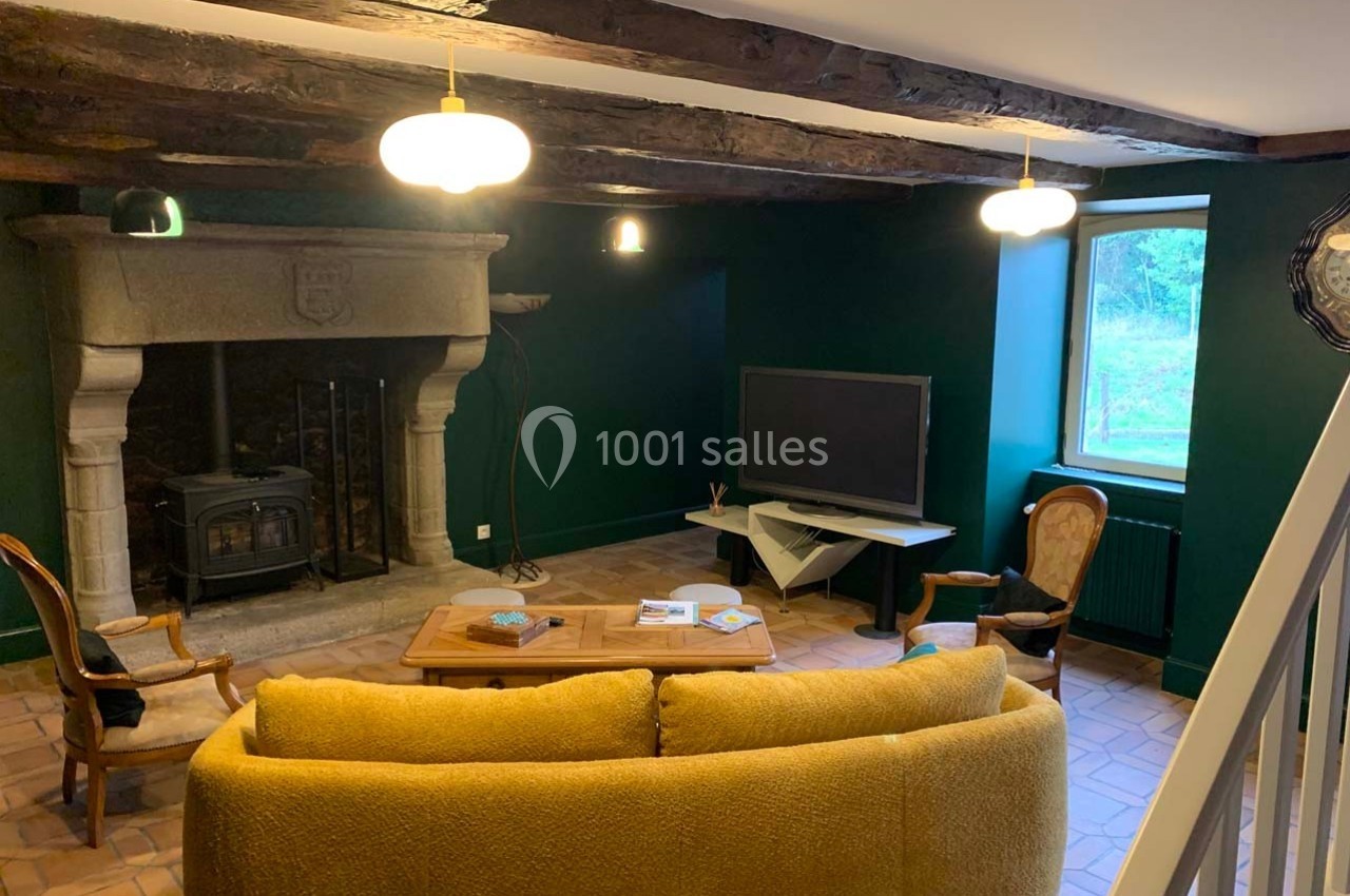 Salon avec murs verts, cheminée en pierre, poêle à bois, canapé jaune, table basse et télévision près d'une fenêtre.