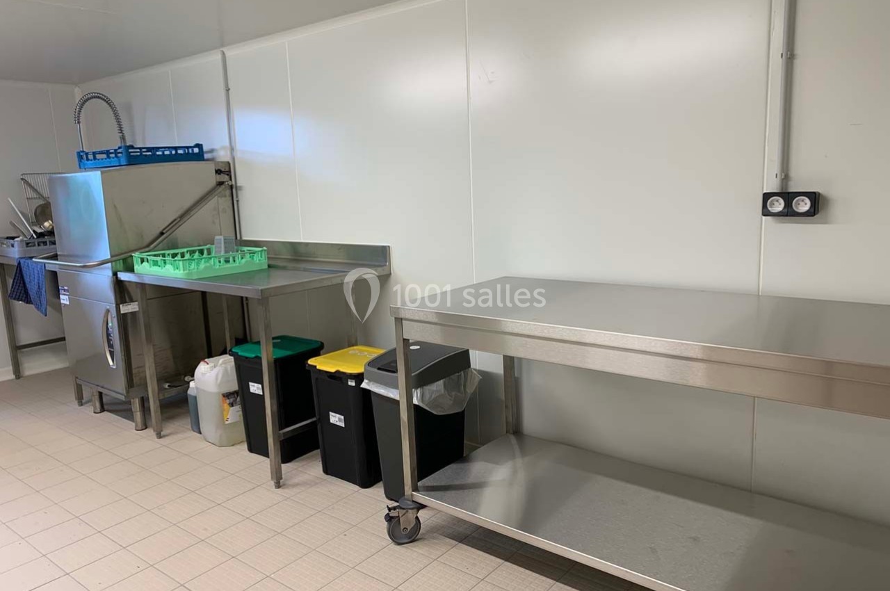 Cuisine professionnelle avec plans de travail en inox, lave-vaisselle industriel, poubelles triées et sol carrelé.