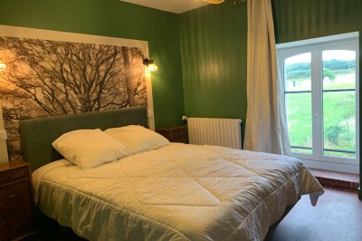 Chambre avec un lit double, murs verts, grande fenêtre donnant sur un paysage champêtre et éclairage doux.