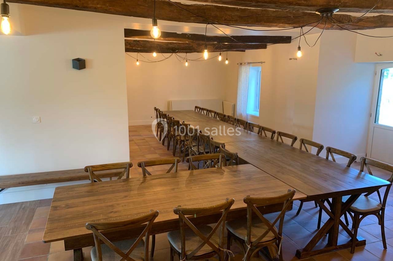 Salle lumineuse avec de longues tables en bois, chaises assorties et poutres apparentes au plafond.