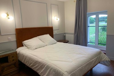 Chambre avec un lit double, murs verts, grande fenêtre donnant sur un paysage champêtre et éclairage doux.