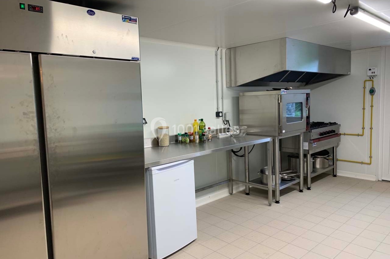 Cuisine professionnelle avec réfrigérateurs, plan de travail en inox, four, hotte et équipements de préparation.