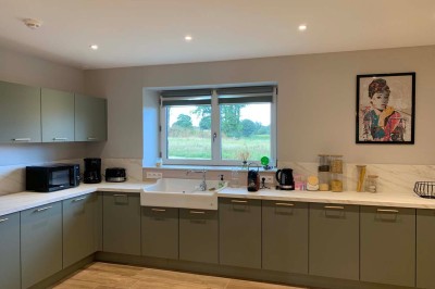 Chambre avec un lit double, murs verts, grande fenêtre donnant sur un paysage champêtre et éclairage doux.