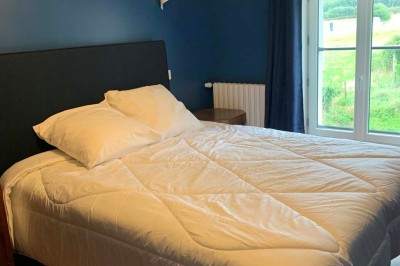 Chambre avec un lit double, murs verts, grande fenêtre donnant sur un paysage champêtre et éclairage doux.