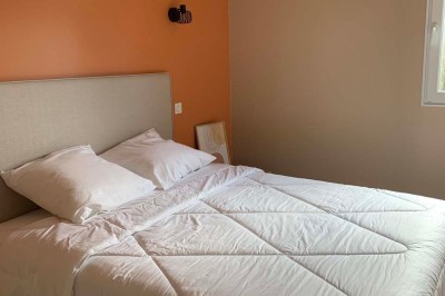 Chambre avec un lit double, murs verts, grande fenêtre donnant sur un paysage champêtre et éclairage doux.