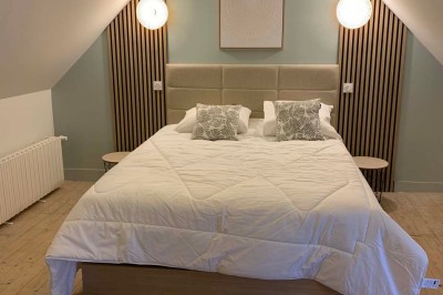 Chambre avec un lit double, murs verts, grande fenêtre donnant sur un paysage champêtre et éclairage doux.