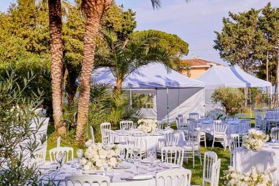 Coussin brodé ’Villa Alexandra’ au premier plan, banc en bois flou en arrière-plan dans un jardin ensoleillé.