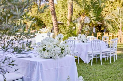 Coussin brodé ’Villa Alexandra’ au premier plan, banc en bois flou en arrière-plan dans un jardin ensoleillé.