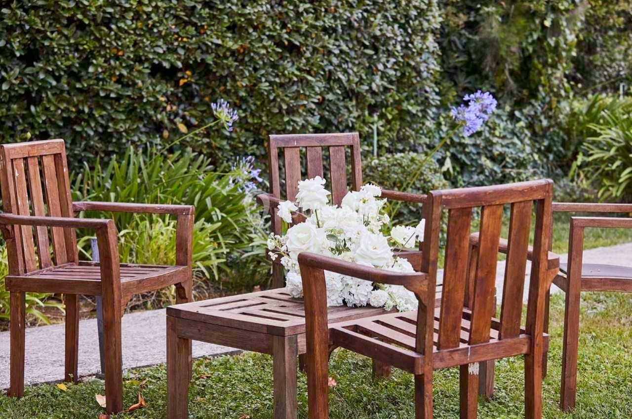 Chaises en bois disposées autour d'une table basse avec un bouquet de fleurs blanches, dans un jardin verdoyant.
