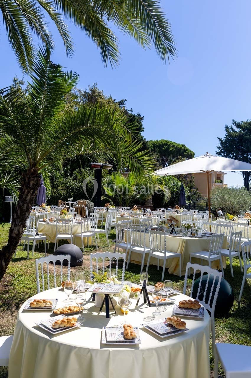 Tables dressées en extérieur avec nappes jaunes, chaises blanches, plats servis et palmiers en arrière-plan.
