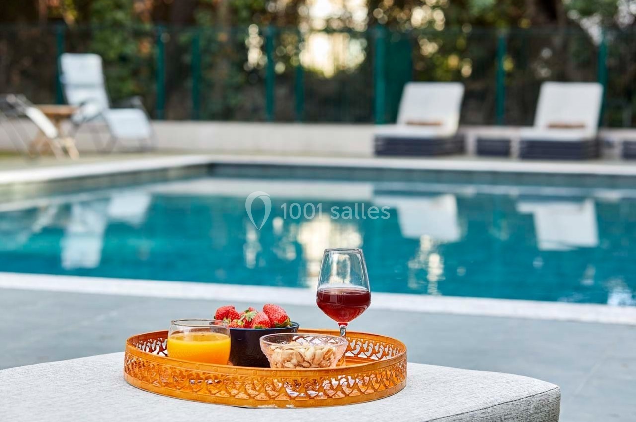 Plateau avec jus d'orange, fraises, noix et verre de vin rouge posé près d'une piscine avec chaises longues en arrière-plan.