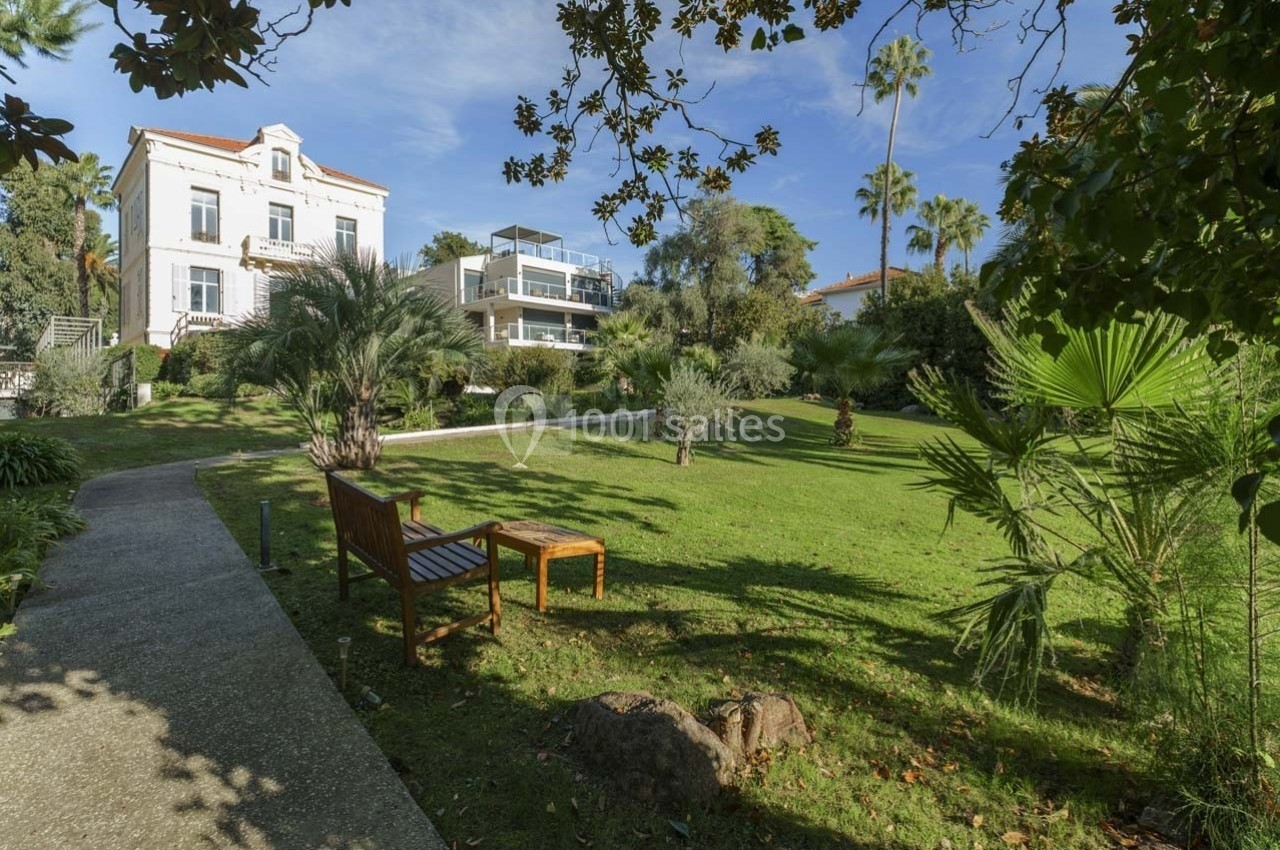 Jardin verdoyant avec banc en bois, allée pavée et bâtiment résidentiel blanc en arrière-plan.