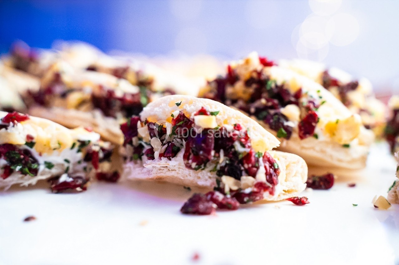 Tranches de pain garnies de fromage, canneberges séchées, noix hachées et herbes, présentées sur une surface blanche.
