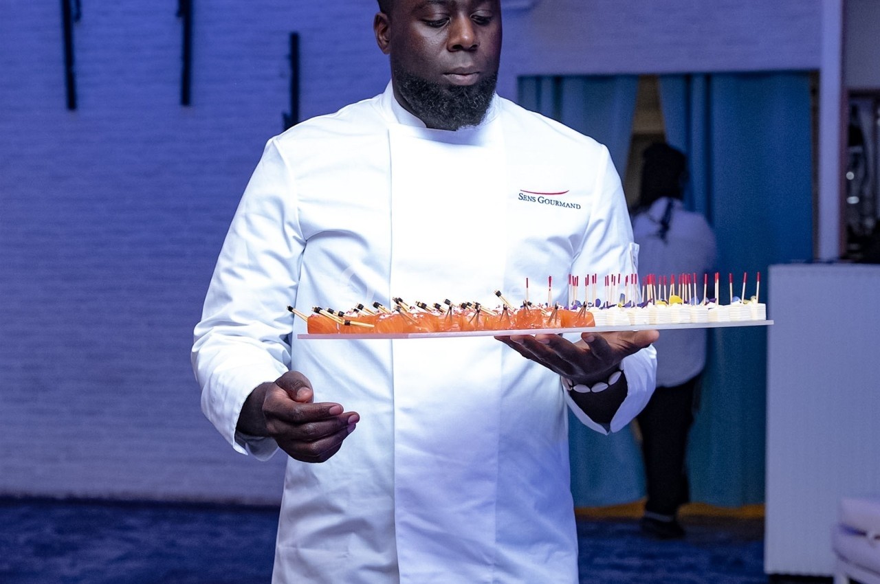 Un serveur en veste blanche porte un plateau de bouchées apéritives dans un espace intérieur éclairé en bleu.