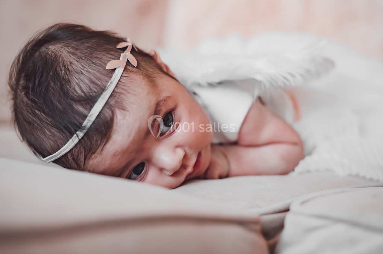 Bébé allongé sur un canapé, portant un bandeau avec un petit nœud et des ailes blanches en tissu.
