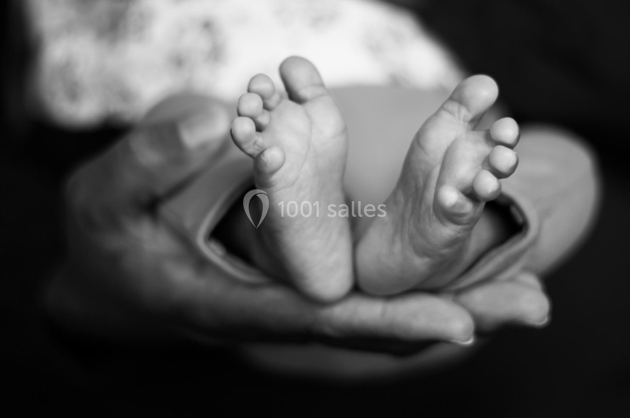 Pieds d'un nouveau-né posés dans les mains d'un adulte, capturés en noir et blanc.