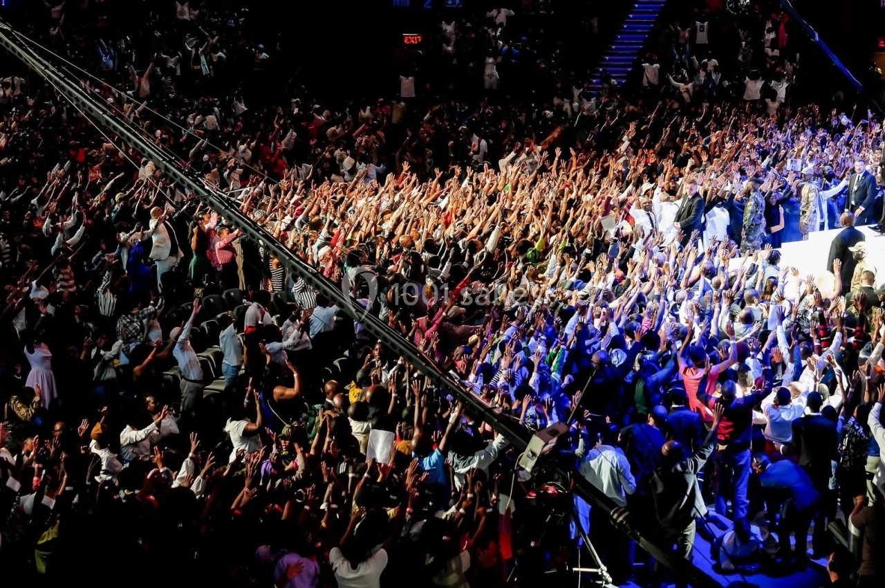Foule dense levant les bras lors d'un événement dans une grande salle éclairée.