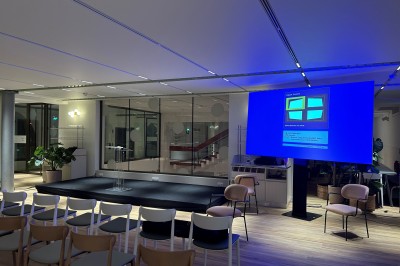 Salle spacieuse avec parquet clair, tables hautes recouvertes de nappes vertes et grandes baies vitrées en arrière-plan.