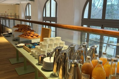 Salle spacieuse avec parquet clair, tables hautes recouvertes de nappes vertes et grandes baies vitrées en arrière-plan.