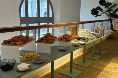 Salle spacieuse avec parquet clair, tables hautes recouvertes de nappes vertes et grandes baies vitrées en arrière-plan.