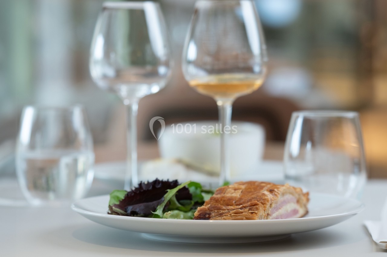 Assiette contenant une part de feuilleté et une salade verte, posée sur une table avec des verres vides et remplis.