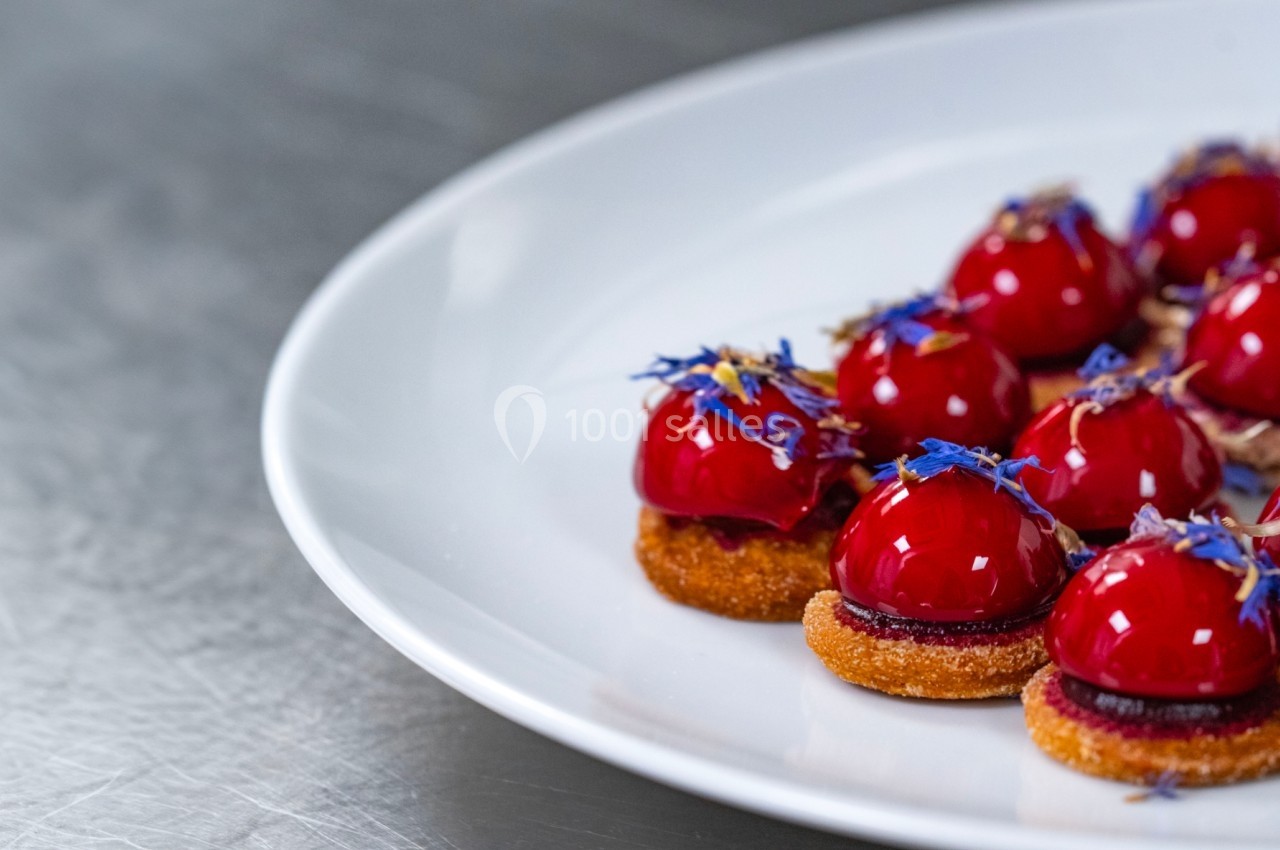 Assortiment de petits desserts rouges glacés sur une base croustillante, décorés de fleurs comestibles.