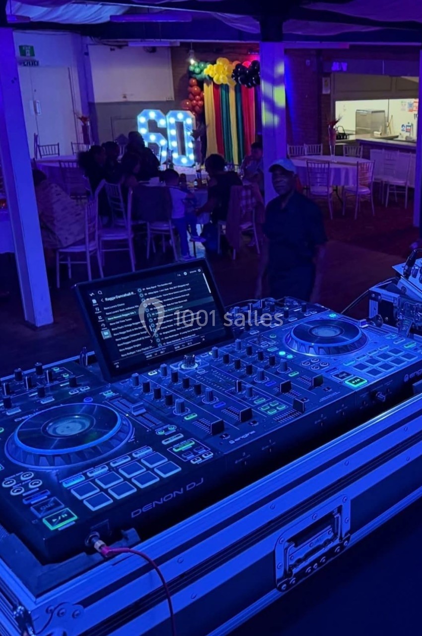Table de mixage Denon DJ éclairée en bleu dans une salle de fête avec décorations colorées et invités en arrière-plan.