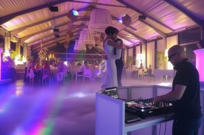 Un couple danse sous des lumières colorées dans une salle décorée, avec un DJ jouant de la musique au premier plan.