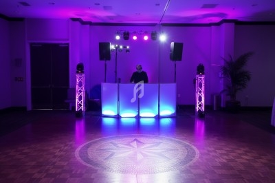 Un DJ mixe derrière une table lumineuse dans une salle sombre éclairée par des lumières violettes.