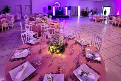 Salle de réception décorée avec des tables rondes élégantes, nappes roses, vaisselle soignée et éclairage tamisé.