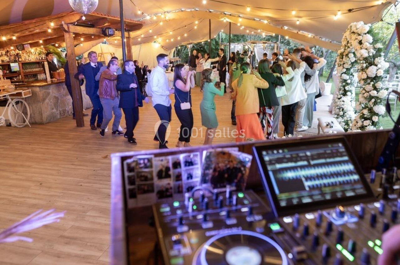 Invités dansant sous une tente éclairée lors d'une réception, avec une table de mixage en premier plan.