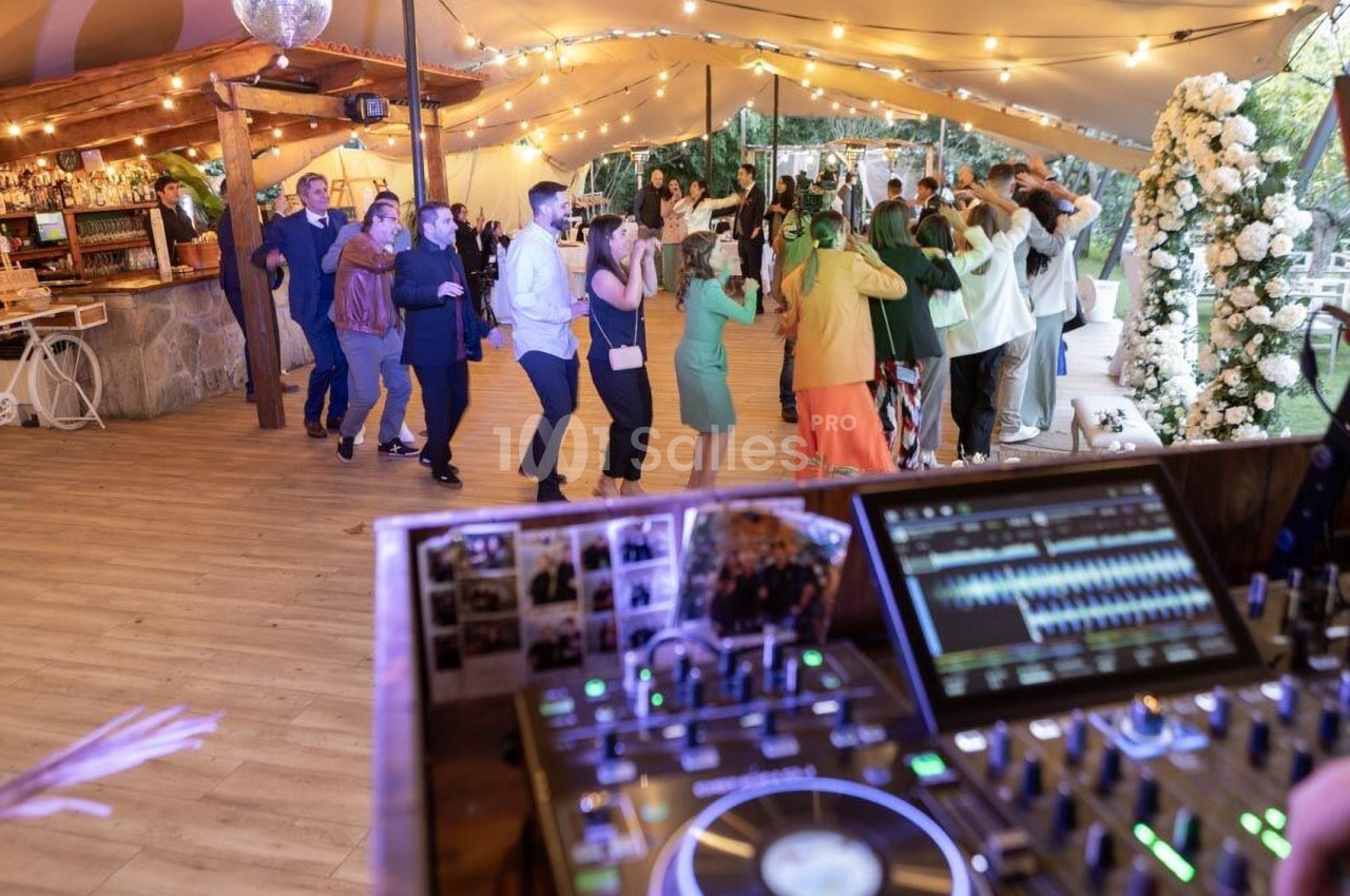 Invités dansant sous une tente éclairée lors d'une réception, avec une table de mixage en premier plan.