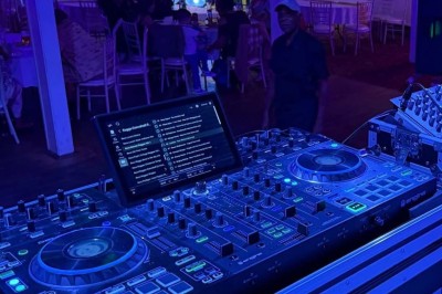 Table de mixage Denon DJ éclairée en bleu dans une salle de fête avec décorations colorées et invités en arrière-plan.