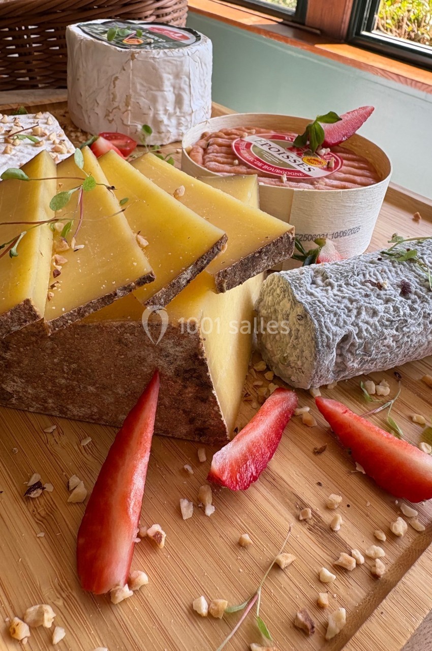 Plateau en bois avec fromages variés, fraises fraîches, noix concassées et herbes décoratives près d'une fenêtre.