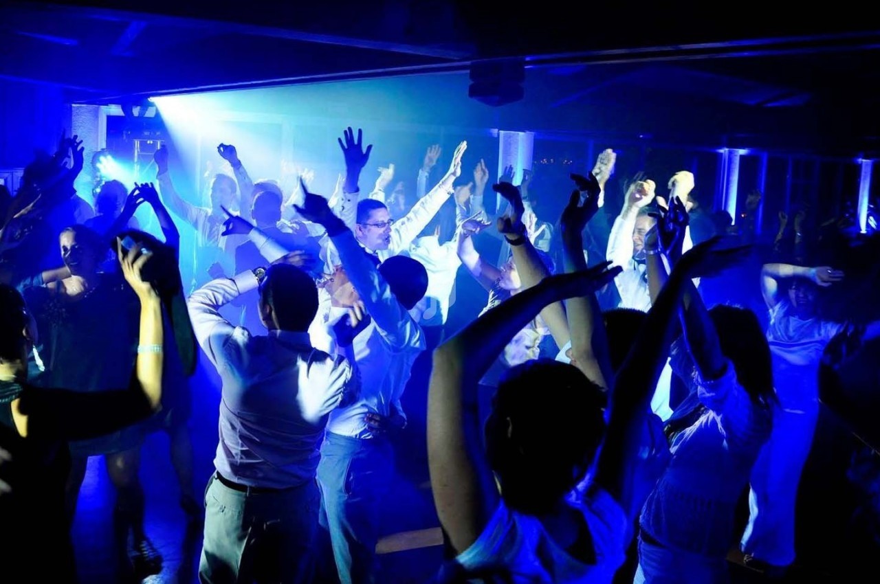Groupe de personnes dansant sous des lumières bleues dans une ambiance festive en intérieur.