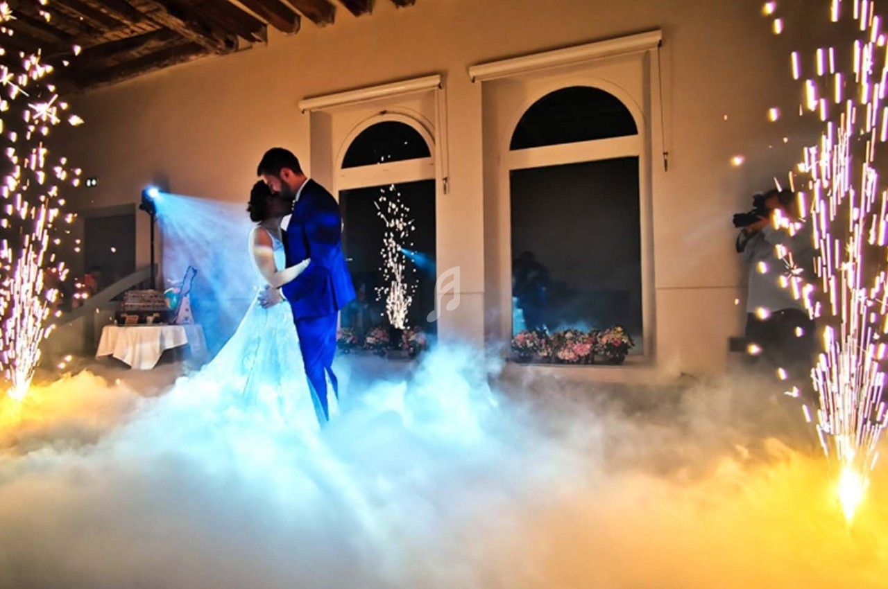 Un couple danse au milieu d'effets de fumée et d'étincelles dans une salle décorée avec des fenêtres et des fleurs.