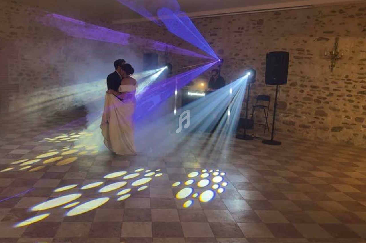Un couple danse sous des jeux de lumière colorés dans une salle en pierre avec un DJ en arrière-plan.