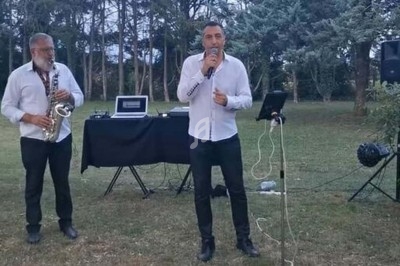 Deux musiciens jouent en plein air, l'un au saxophone et l'autre chante avec un micro devant un équipement audio.