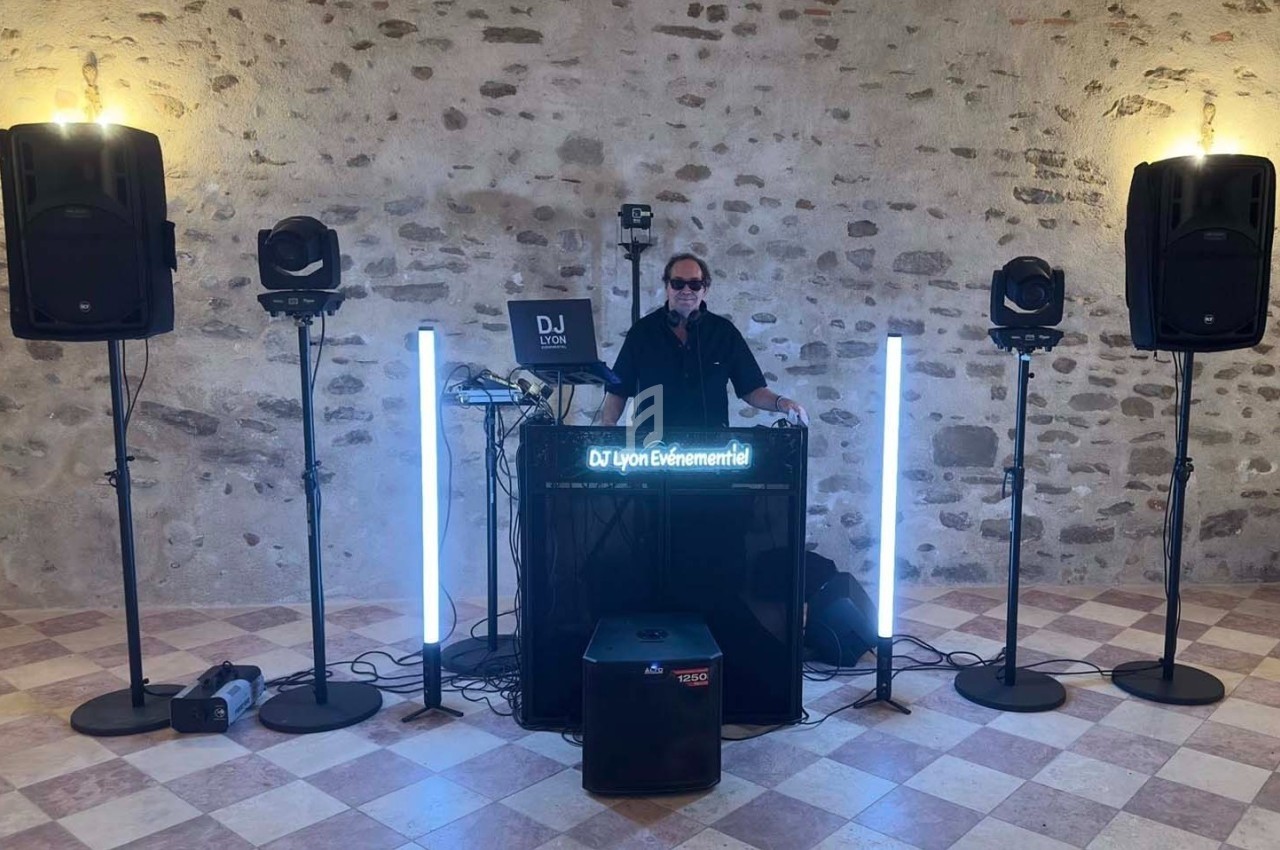 Un DJ derrière une table de mixage avec éclairage LED, entouré de haut-parleurs dans une salle en pierre.