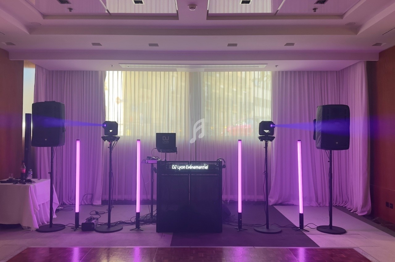Installation de matériel de sonorisation et éclairage violet dans une salle avec rideaux blancs et parquet au sol.