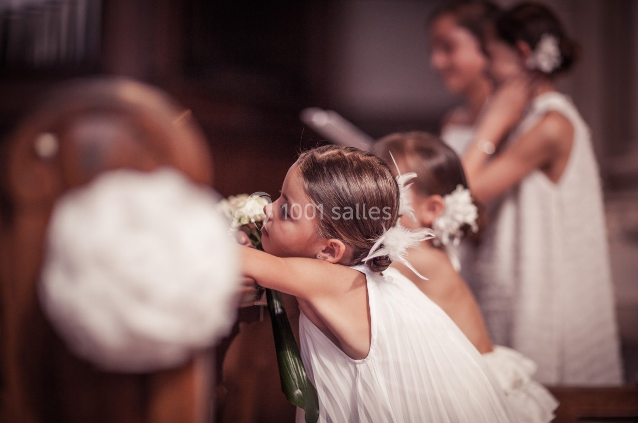Une jeune fille en robe blanche appuyée sur un banc, entourée d'autres enfants lors d'une cérémonie.