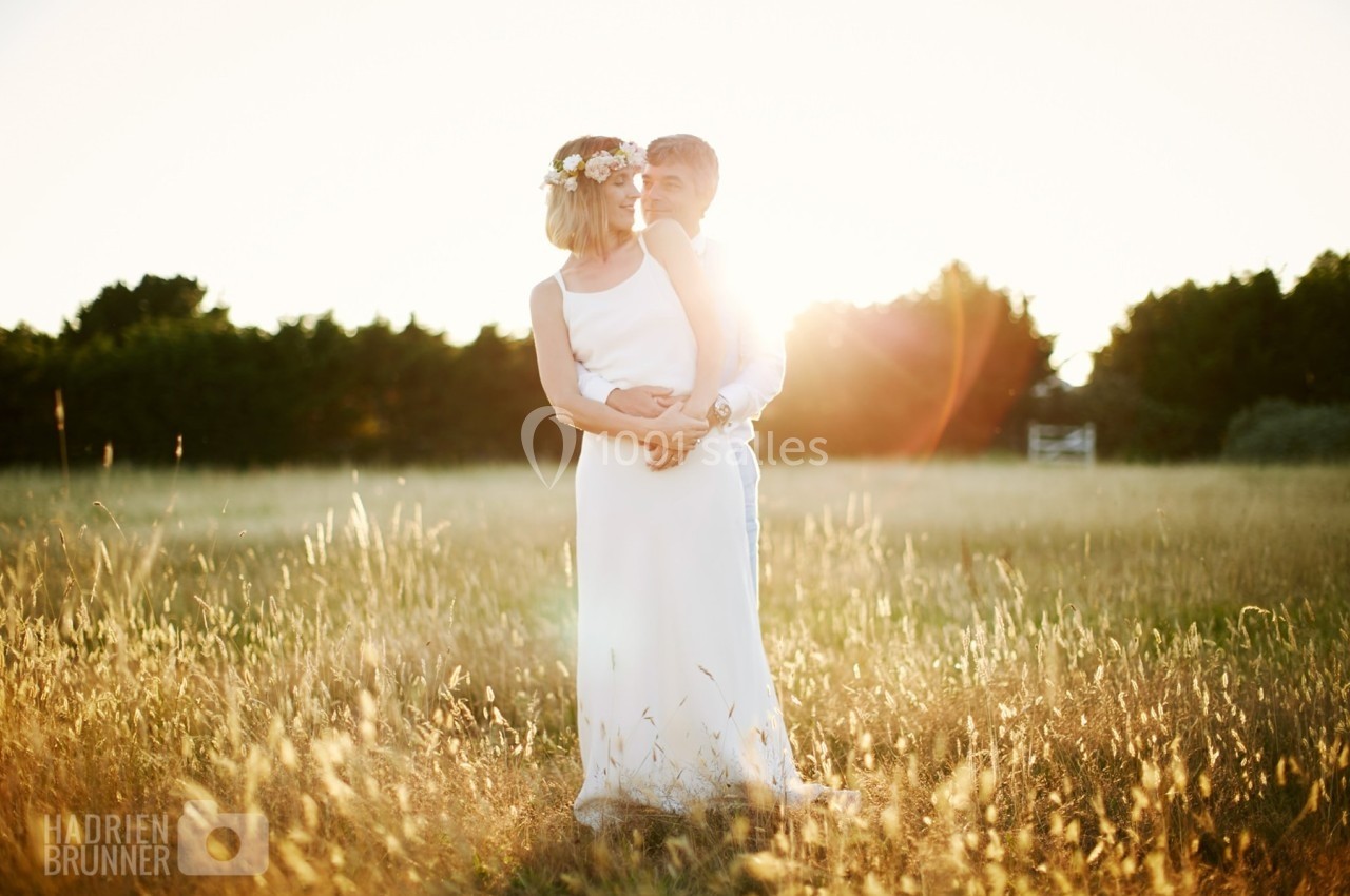 Un couple habillé en tenue de mariage se tient dans un champ ensoleillé, entouré d'herbes hautes.