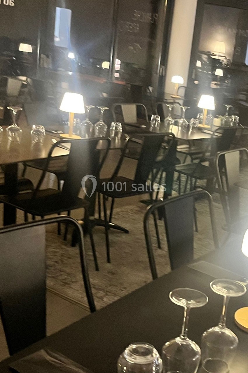 Salle de restaurant moderne avec tables dressées, chaises noires et lampes de table diffusant une lumière douce.
