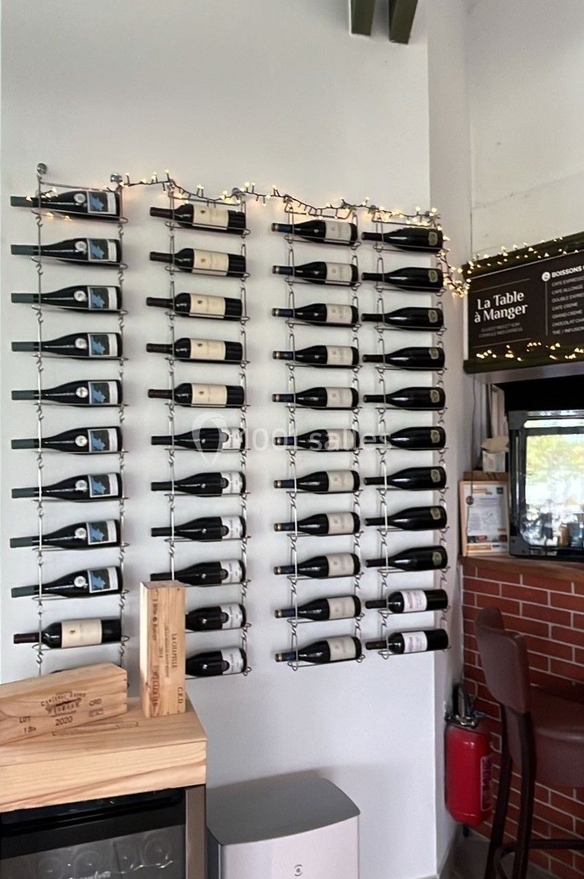 Mur avec des bouteilles de vin alignées sur des supports métalliques, décoré de guirlandes lumineuses.