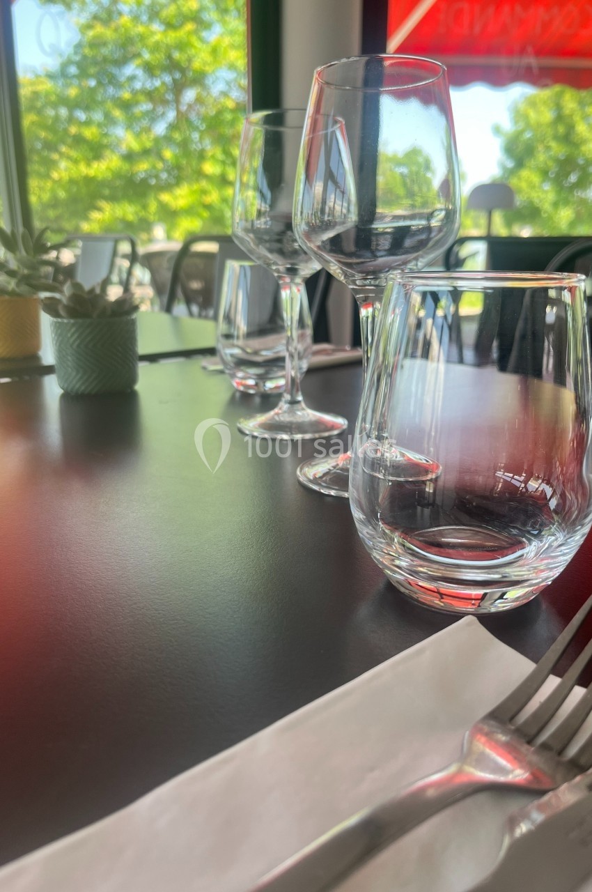 Quatre verres alignés sur une table noire avec des couverts, des plantes décoratives et une vue sur l'extérieur.