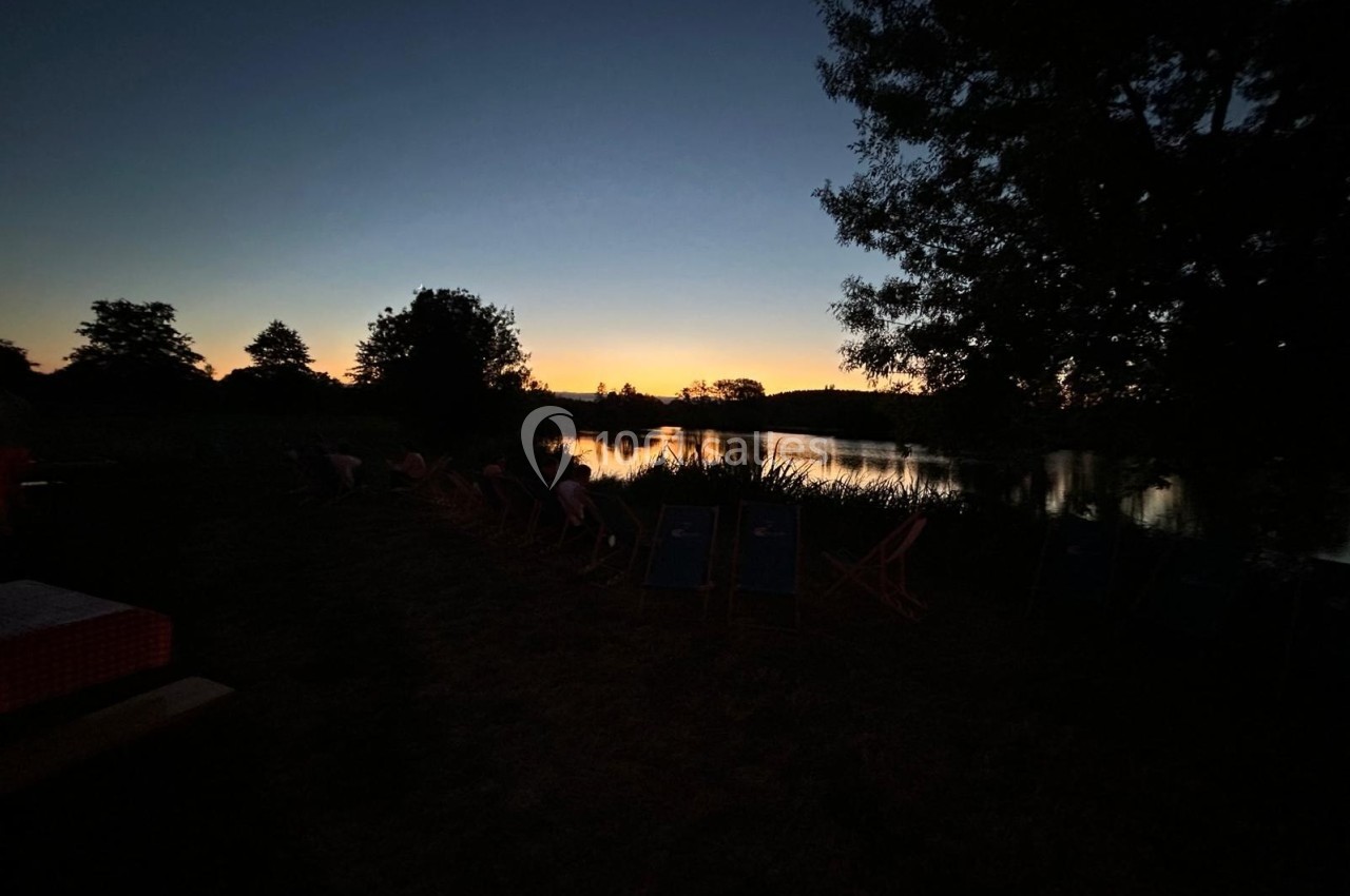 Paysage au crépuscule avec un lac reflétant le ciel, entouré d'arbres et de chaises longues en contre-jour.
