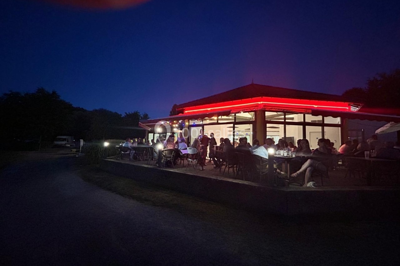 Terrasse d'un restaurant éclairée par des néons rouges, avec des clients attablés en soirée.