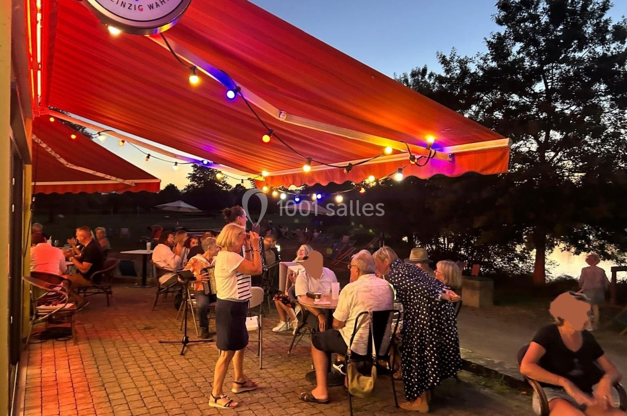 Terrasse éclairée par des guirlandes lumineuses au coucher du soleil, avec des personnes discutant et profitant de l…