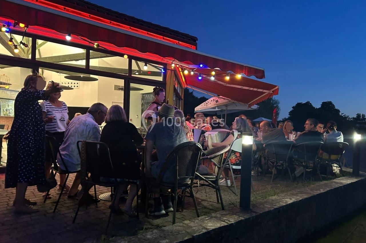 Groupe de personnes assises en terrasse éclairée le soir, discutant sous un auvent rouge avec des lumières colorées.